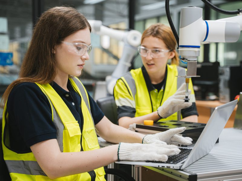 Female,Engineer,Working,On,Laptop,Computer,While,Colleague,Inspecting,Robotic